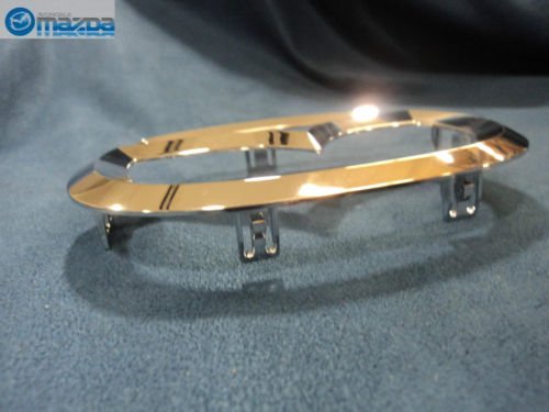 Mazda front logo emblem part, precise alignment for grille aesthetics.
